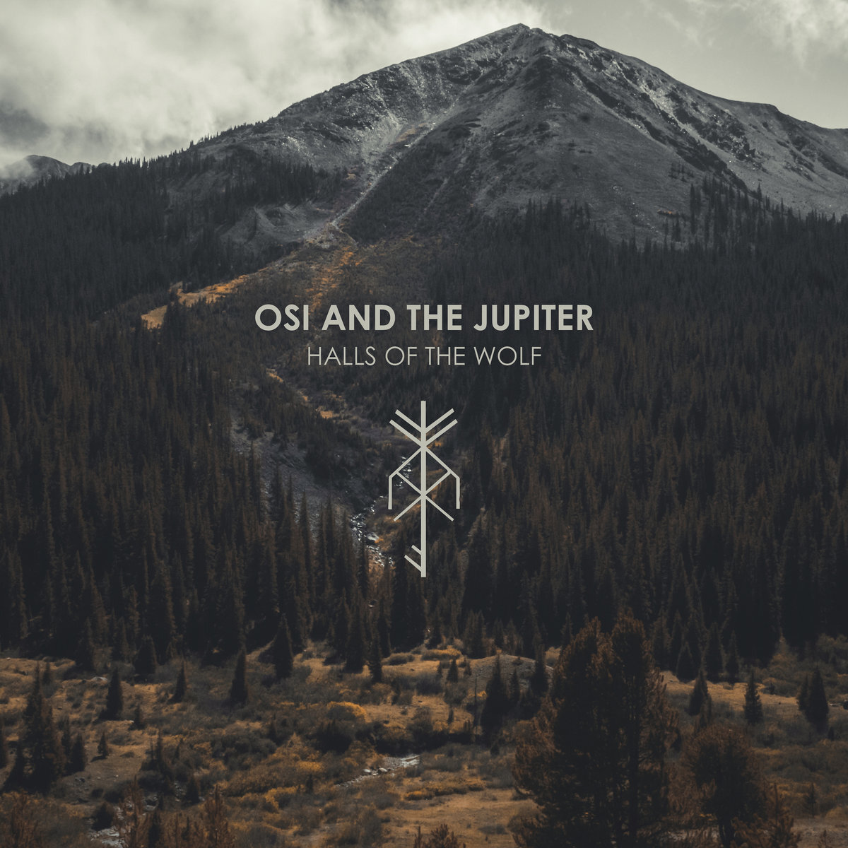 Halls of the Wolf, the album cover made for Osi and The Jupiter. A mountain above a conifer valley under cloud, with the band name and a bind rune set over it.