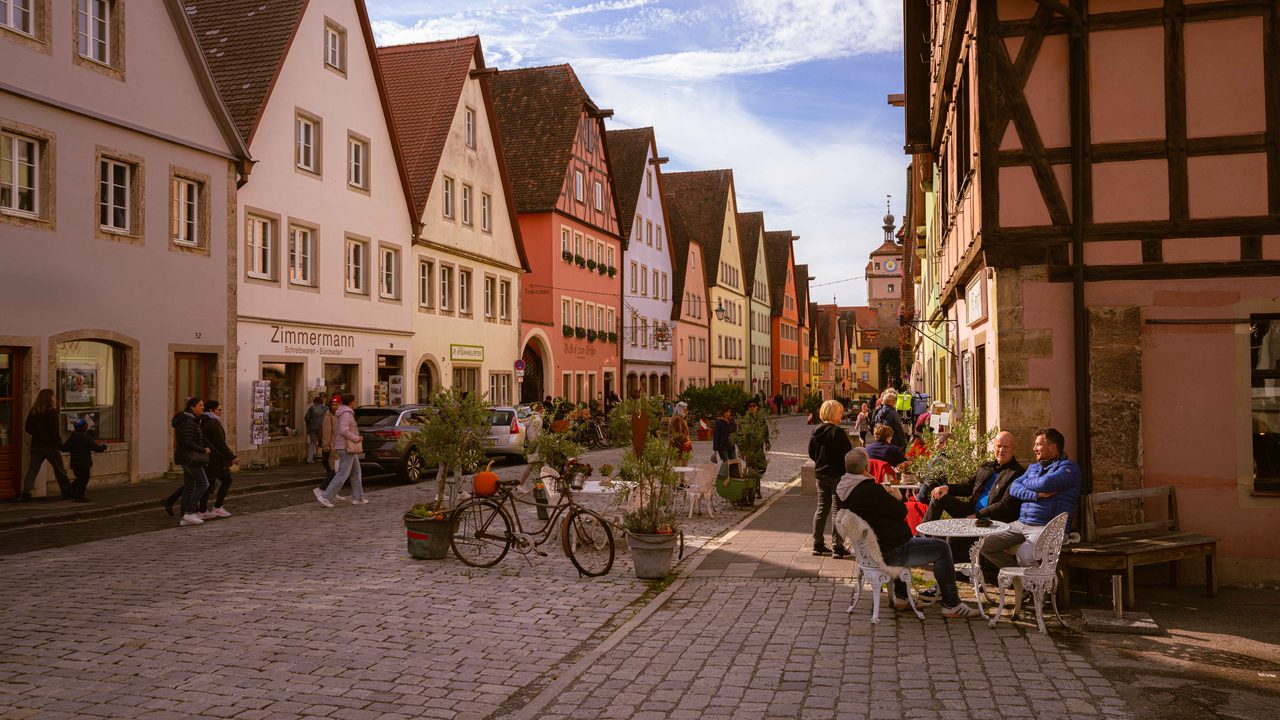 A street of half timbered houses with people at tables.