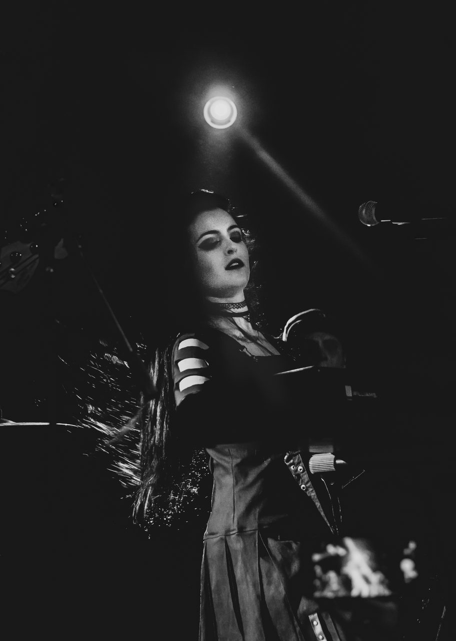 Sharone at the microphone stand, striped sleeves, lit from above.