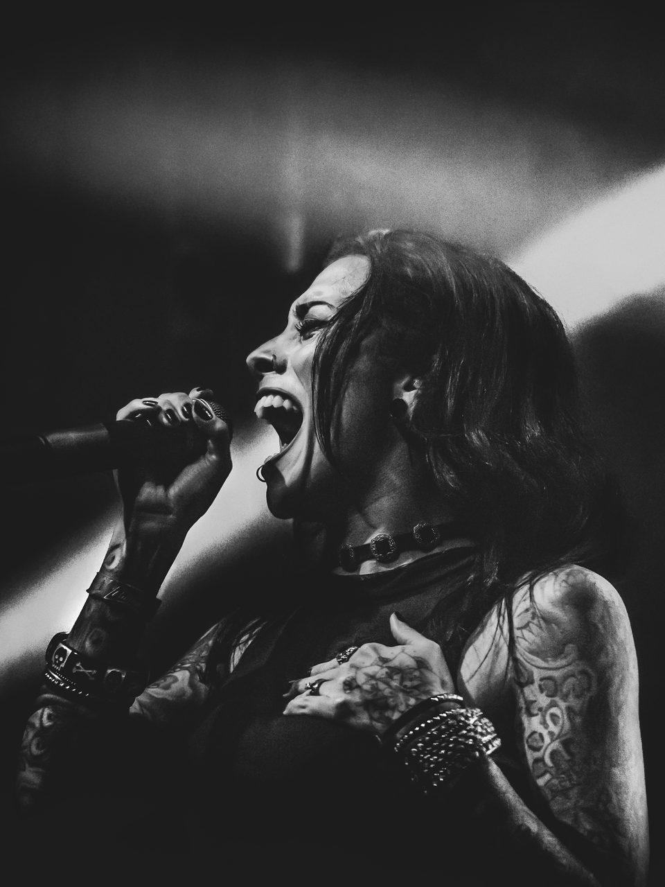 Lola Black screaming into the microphone, tattooed arms raised.