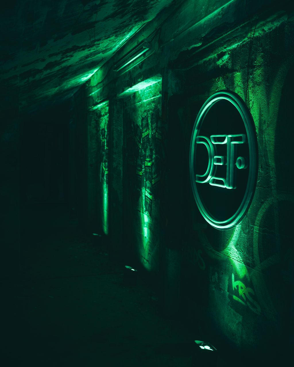 A circular DEF emblem glowing green on a concrete wall at the end of a dark passage.