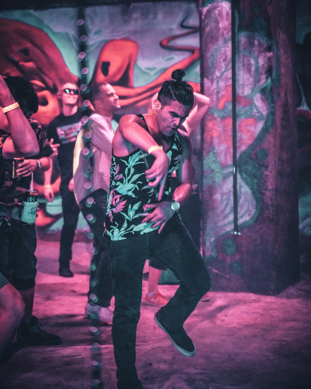 A dancer mid step under pink light in front of a painted octopus, others standing behind him.