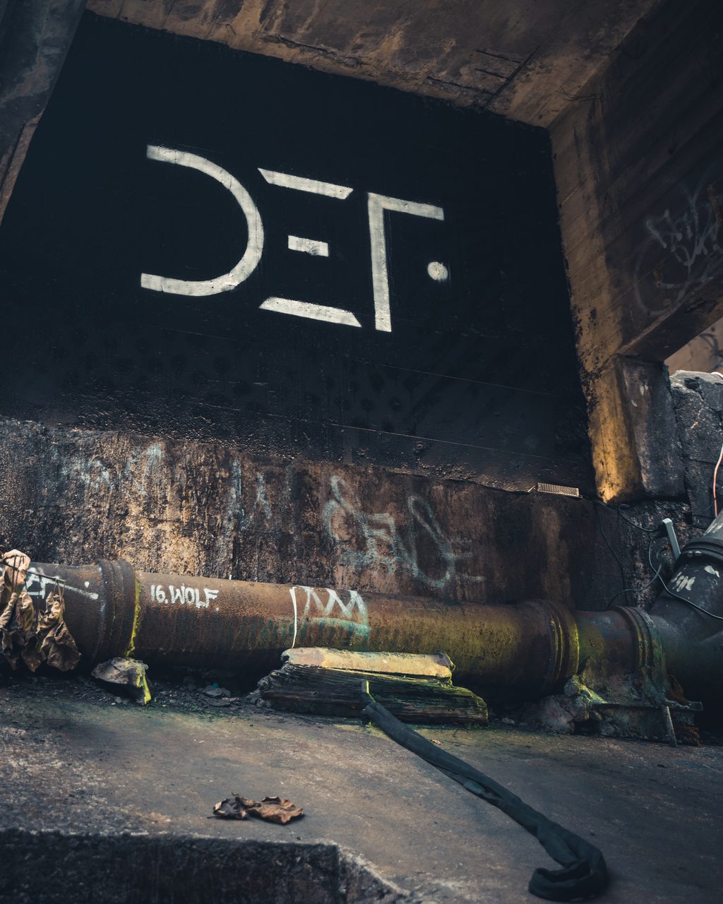 A DEF wordmark painted on a dark panel above a rusted pipe in a concrete undercroft.