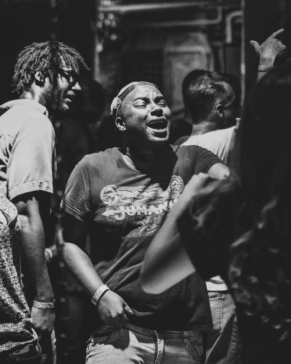 Black and white. A person in the crowd laughing with their head back, others pressed in around them.