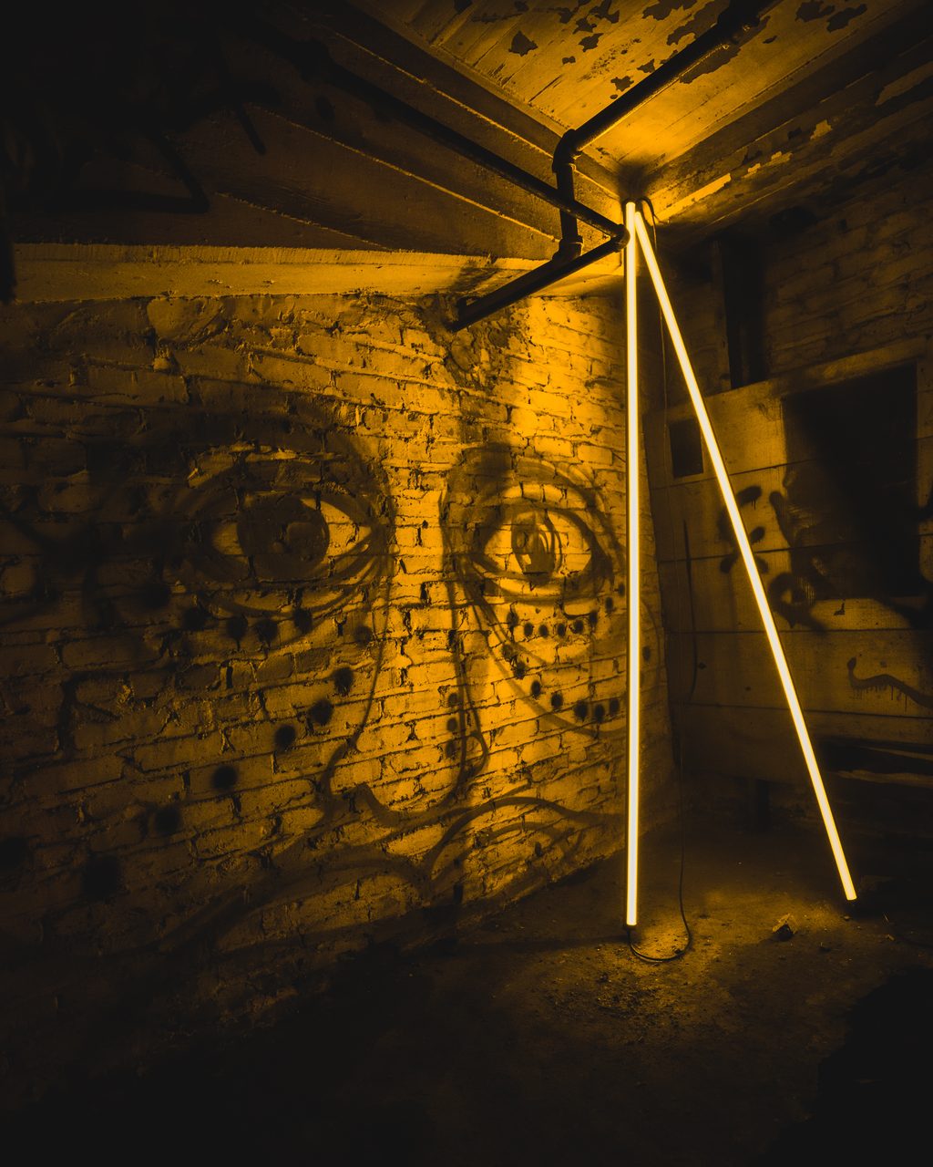 Two lit tubes leaning against a brick wall painted with a large face.