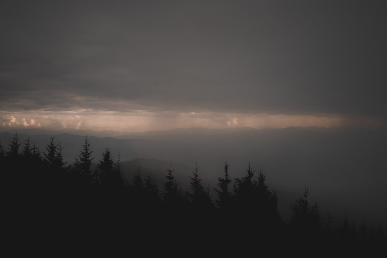 A band of evening light over a dark conifer ridge.