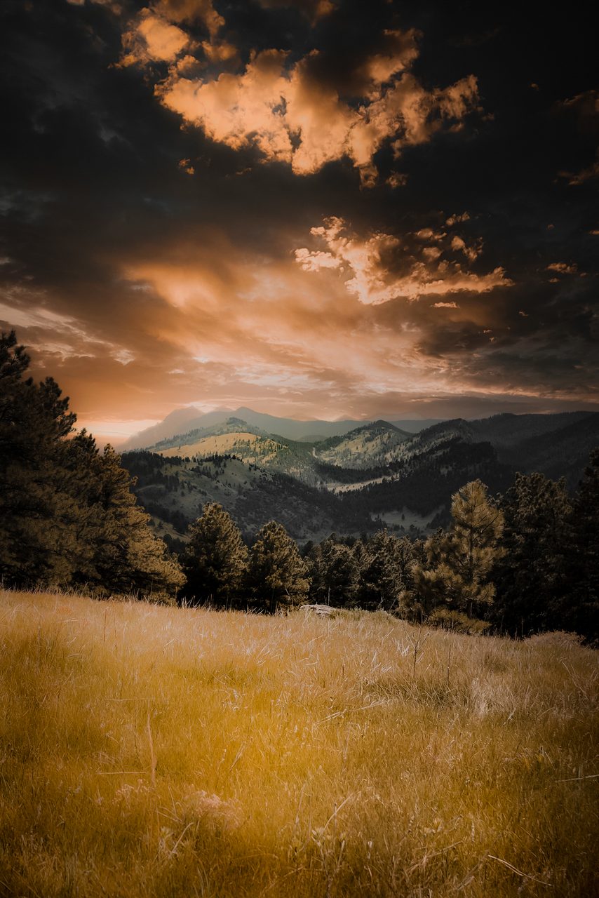Burning cloud over layered ridges, a golden meadow below.