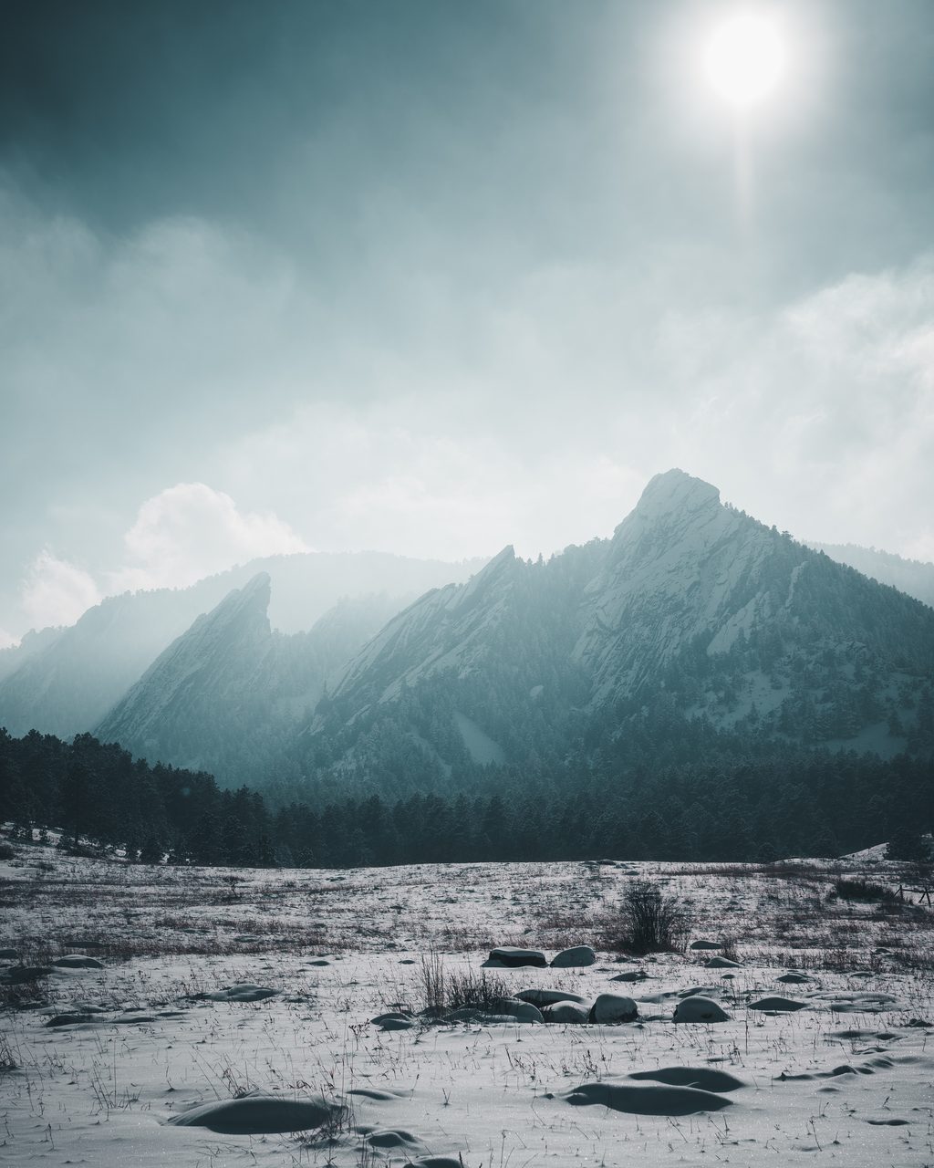 The Flatirons in snow haze under a high white sun.